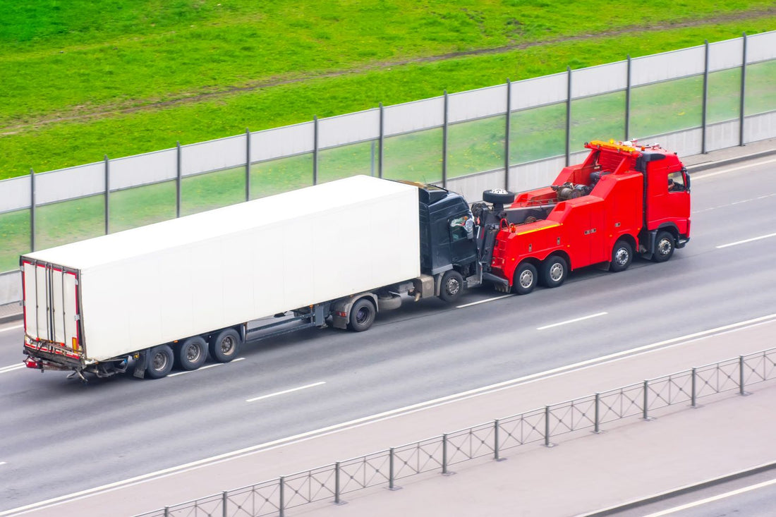 A large, red recovery truck towing a semi-truck along an interstate during the day.