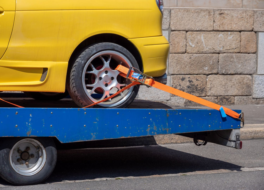 yellow vehicle tied down to blue tow dolly with an orange wheel strap