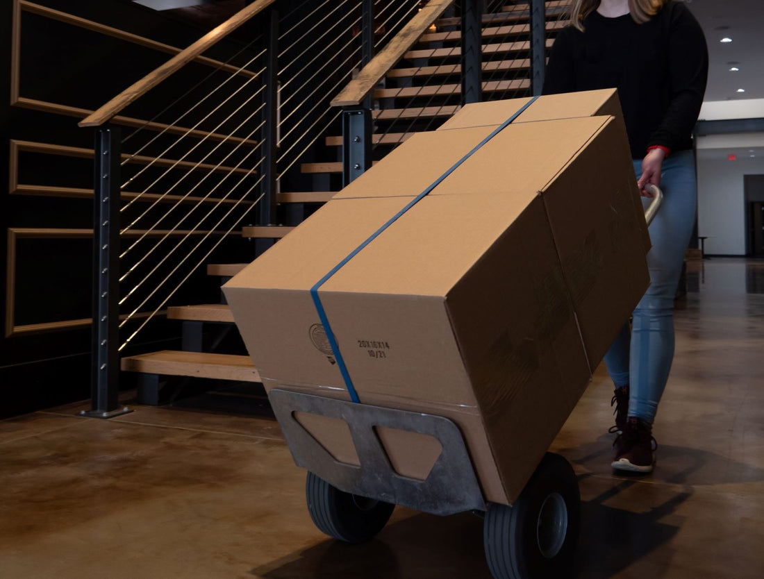 aluminum hand truck moving a stack of cardboard boxes across a warehouse