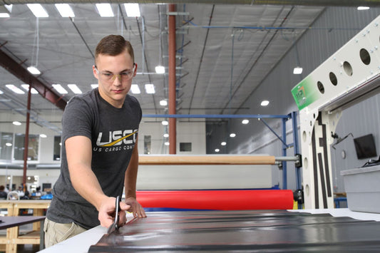 A close-up shot of a USCC manufacturer cutting a custom black lumber tarp inside the warehouse.